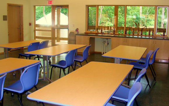 One of our classrooms, with blue chairs arranged in pairs behind tables. The windows look out onto a covered porch and green space.