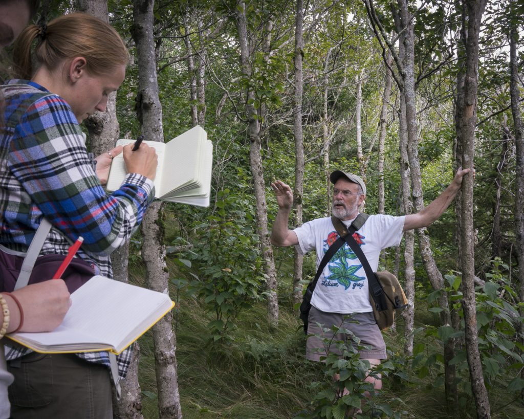 Alan Weakley stands in the woods, leading a class of students using notebooks to take notes