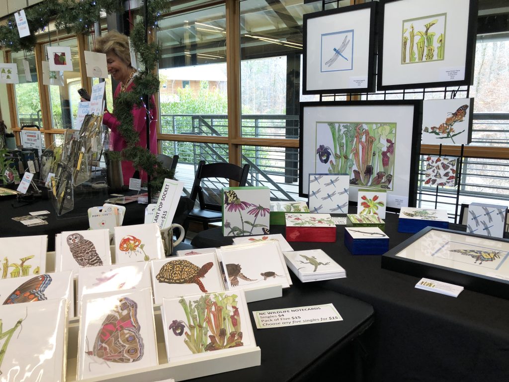 Cards and artwork of native plants and animals by Rebecca Dotterer set up at the 2022 Winter Craft Market inside Reeves Auditorium